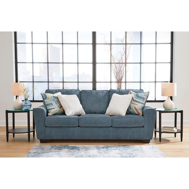 Full front view of the same sofa model, presented in a rich denim blue textured fabric, staged in a similar modern living room environment with end tables and natural decor elements.