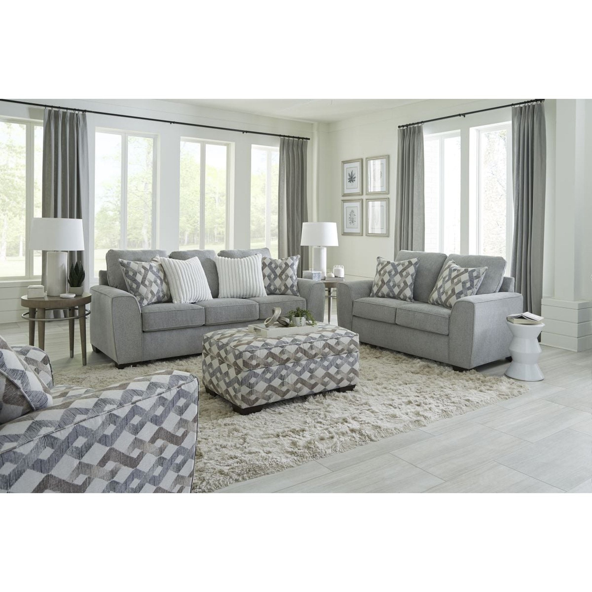 The steel gray loveseat is showcased as part of a complete living room set, featuring its clean lines and two decorative geometric pillows, set in a bright, modern living space.