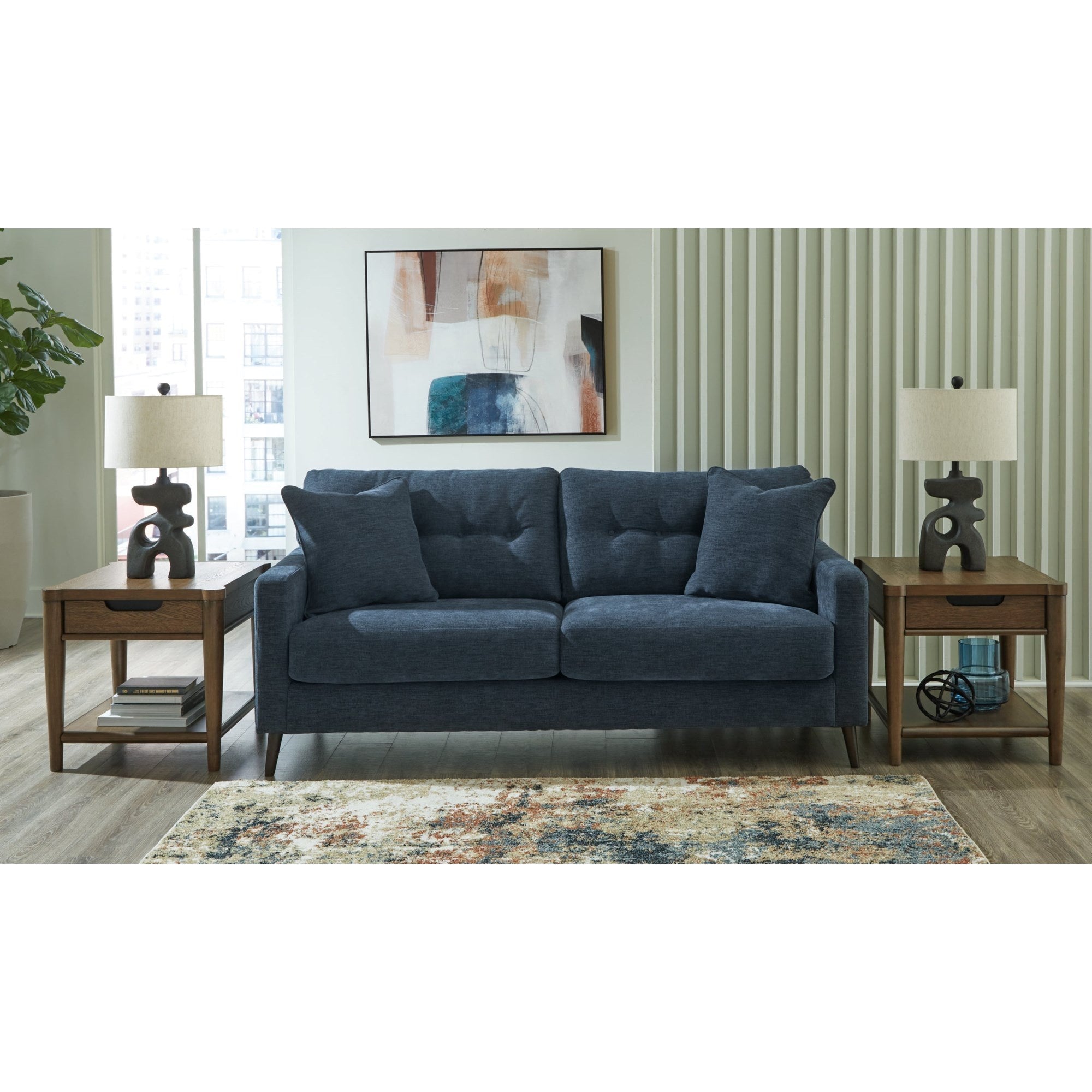 Lifestyle shot of a matching blue sofa, similar in style with button tufting and dark tapered legs, enhancing a modern living room setup with neutral walls and a patterned rug.
