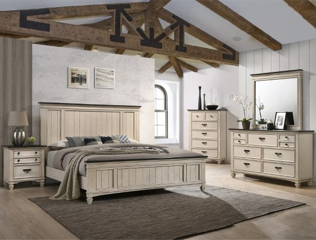 The primary view of the bedroom set, featuring the bed with its plank panel headboard and footboard, alongside a matching nightstand, highlighting the distressed cream finish and dark top accents.